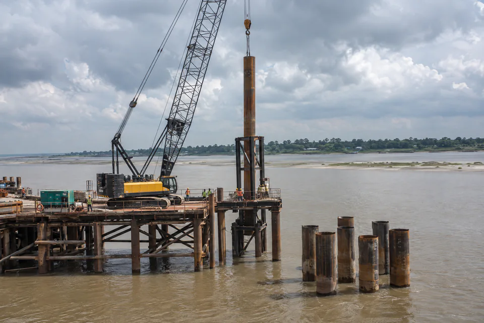 Illustration: a crane lifting a steel pipe pile for a river bridge foundation in Bangladesh