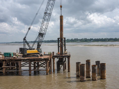 Illustration: a crane lifting a steel pipe pile for a river bridge foundation in Bangladesh
