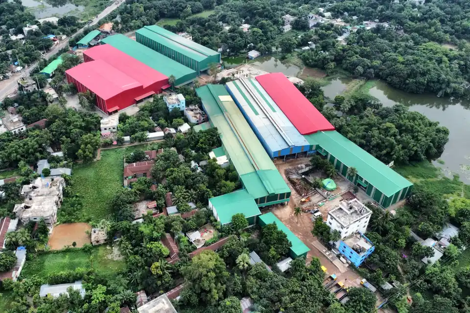 Aerial view of the Gram Bangla Tubes plant campus in Sonargaon, with production sheds among trees beside a lake