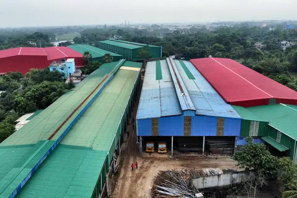 Delivery trucks and steel pipe stock in the yard between production sheds at Gram Bangla Tubes, Sonargaon